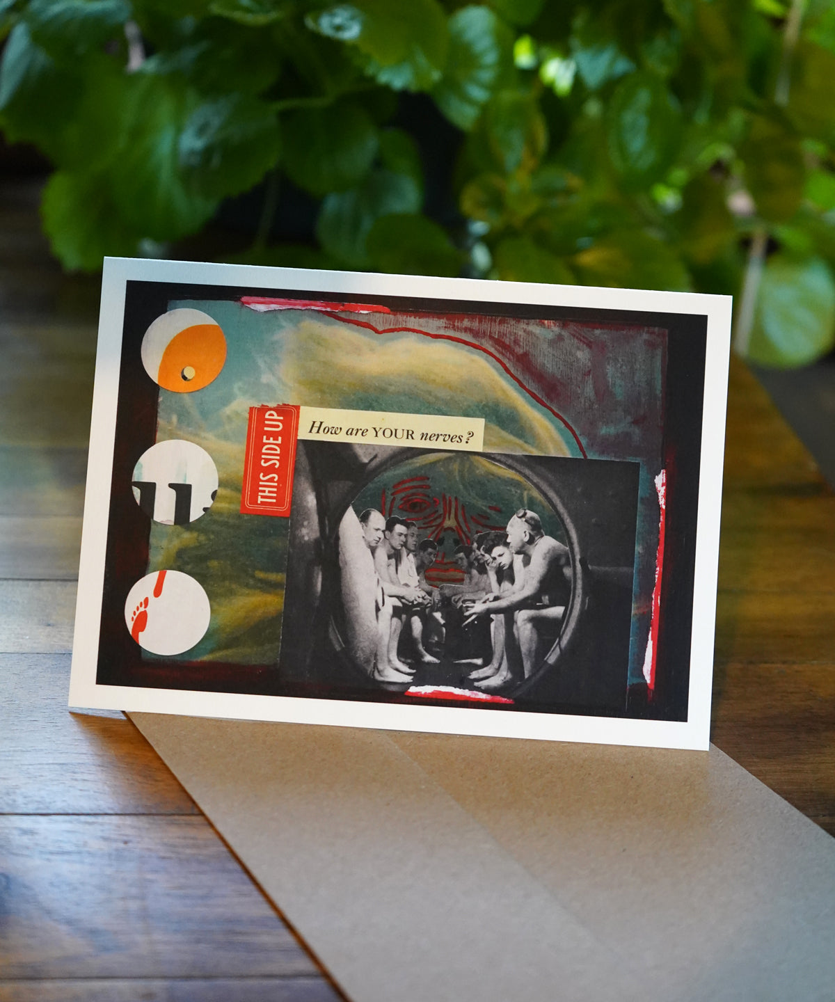 Artistic card with abstract design and text on a wooden surface with greenery in the background