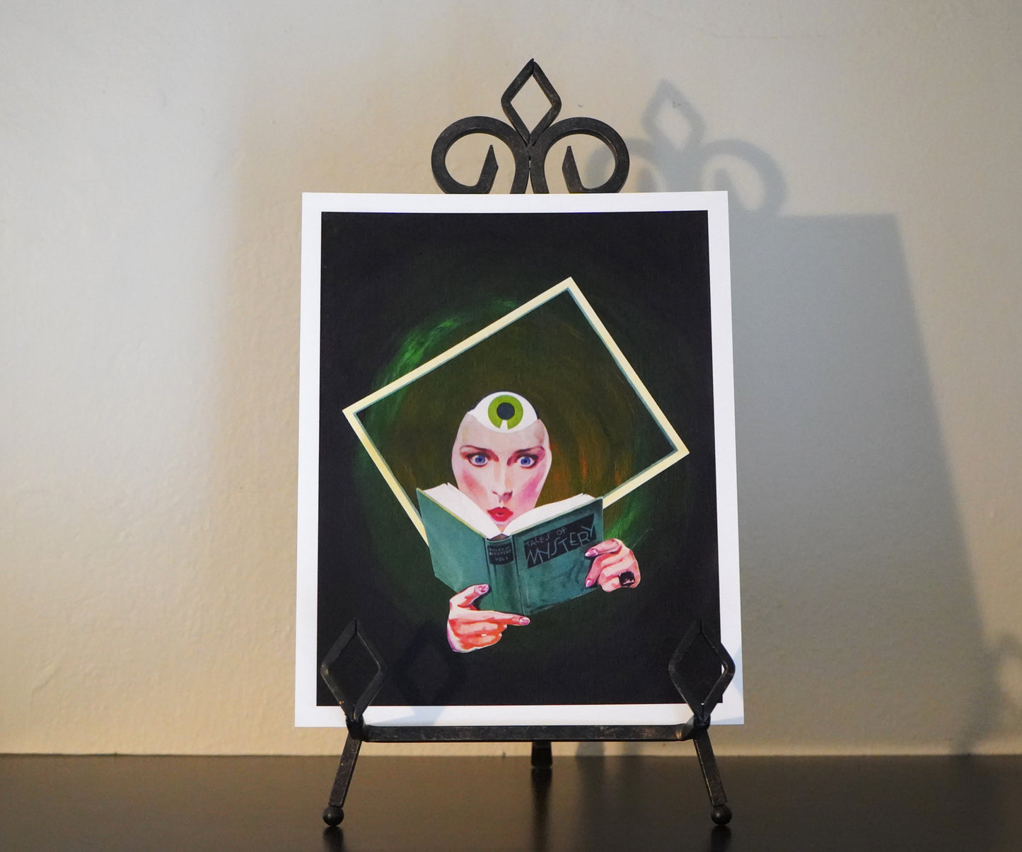 Framed artwork of a woman reading a book on a stand against a plain wall.