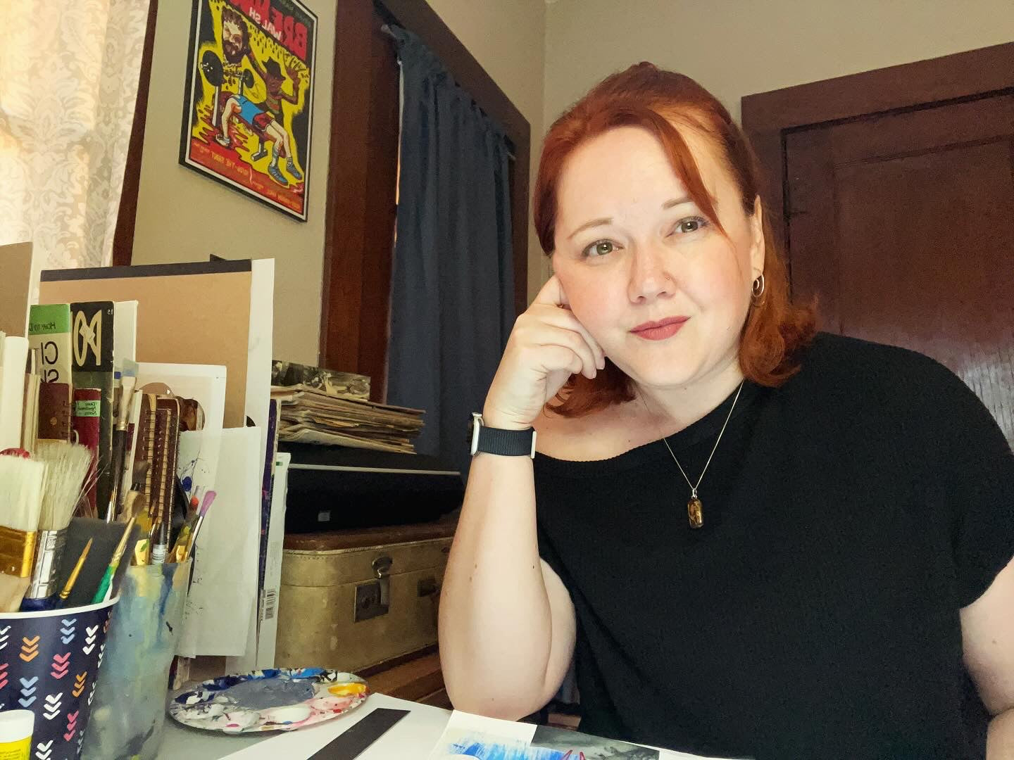 Woman with red hair sitting in a room with books and a painting in the background