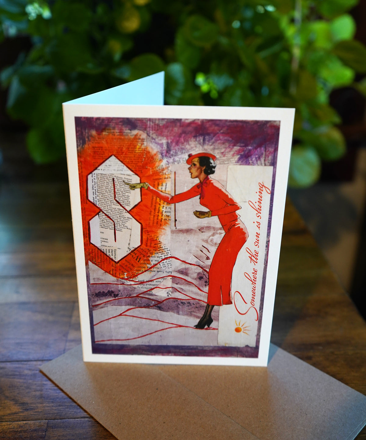 Greeting card with artistic design of a woman in a red dress and an orange 'S' on a wooden surface.